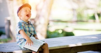 little boy sitting on a bench with a book laughing